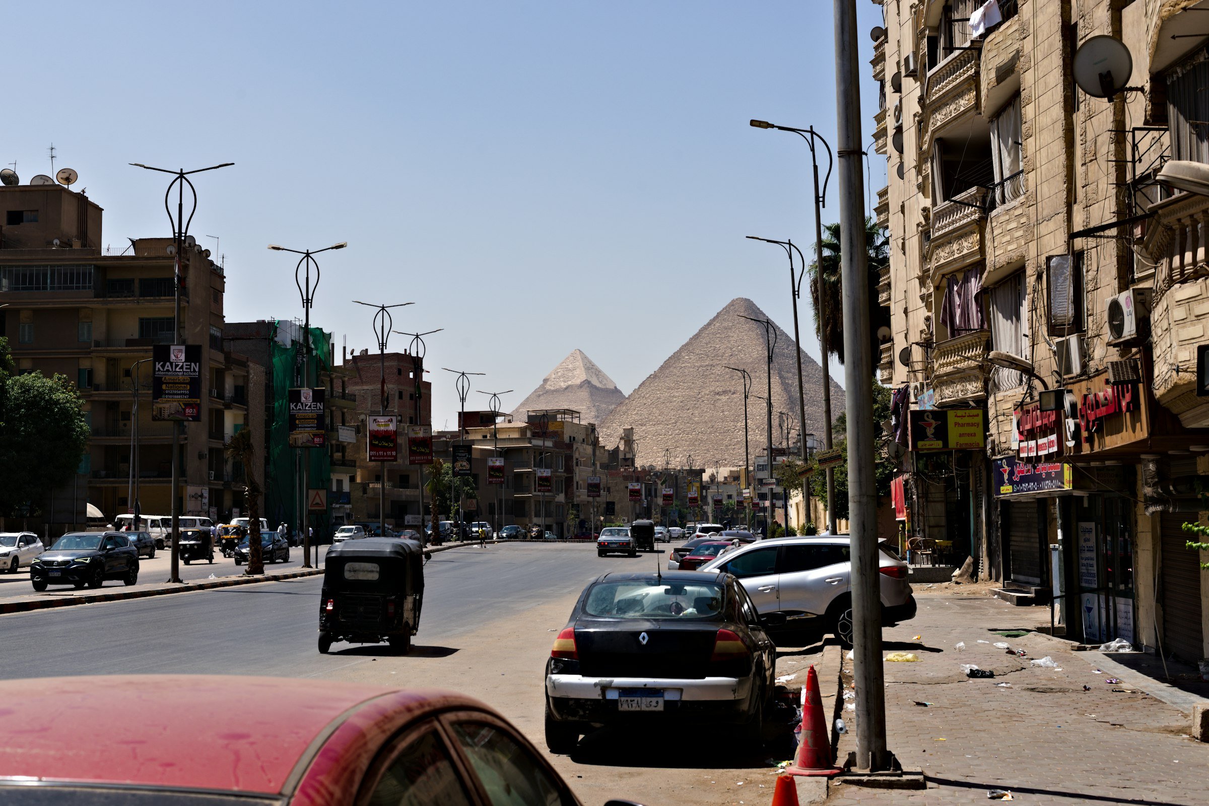 حركة السيارات في شارع بالجيزة مع ظهور الأهرامات خلف المباني